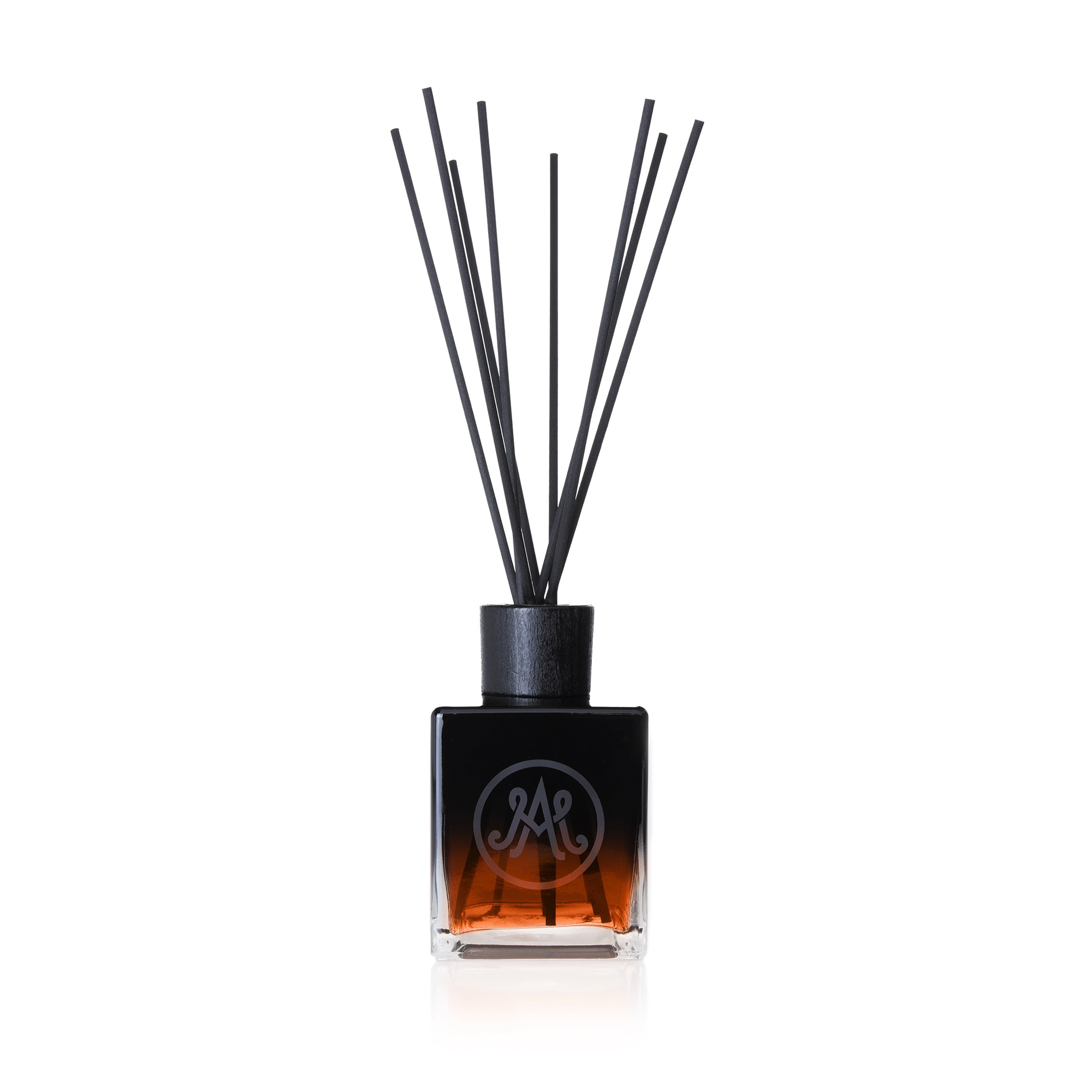 A dark amber diffuser with black reeds is displayed, featuring a sleek black cap and an elegant monogram logo on the front of the bottle. Infused with notes of prunes, apricots, oak, and a touch of Armagnac, this exceptional fruity and spicy fragrance is perfect for both men and women.