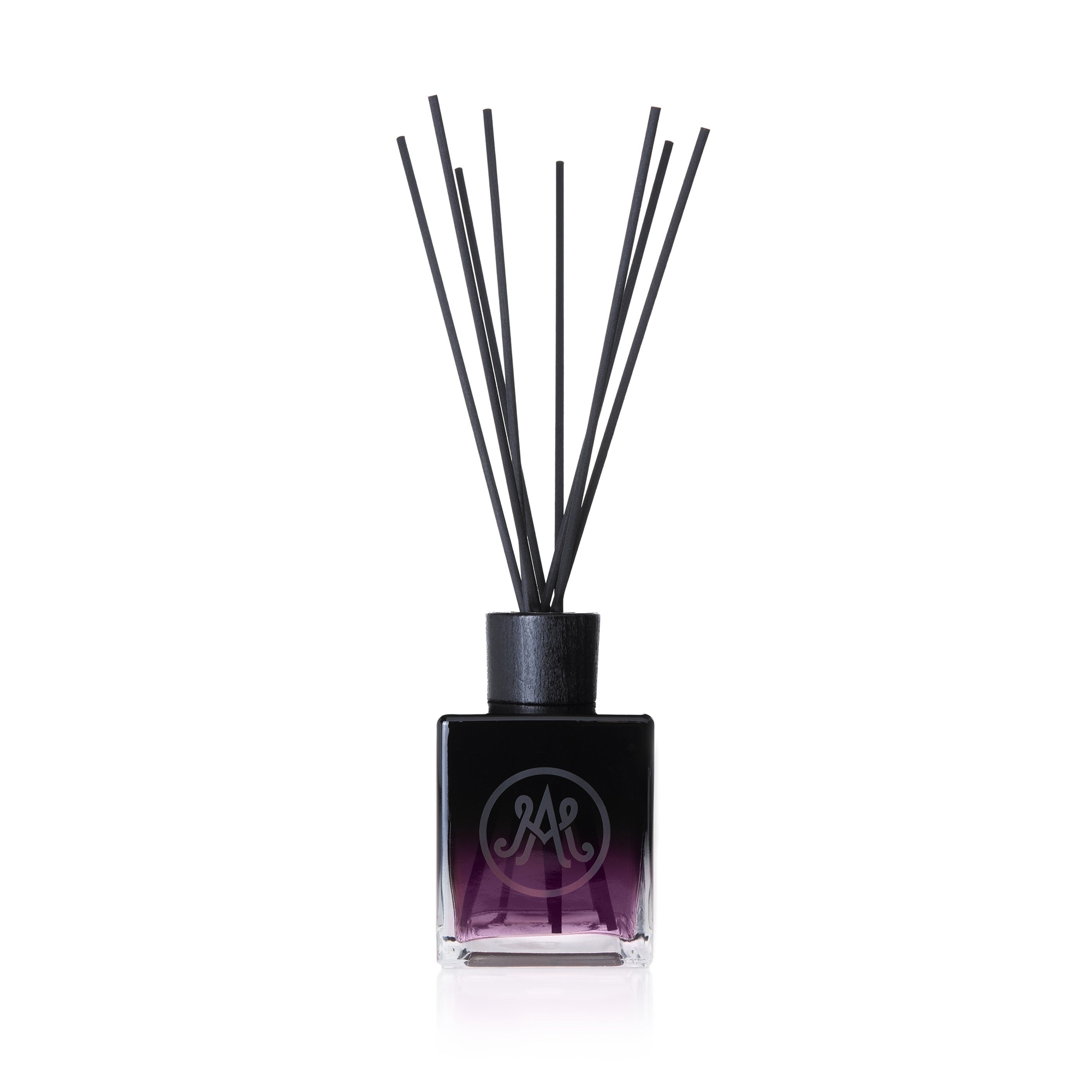 A dark purple diffuser with black reeds is displayed, featuring a sleek black cap and an elegant monogram logo on the front of the bottle. Infused with notes of blackcurrant and raspberry, creating a sweet, deep, and smoky scent.