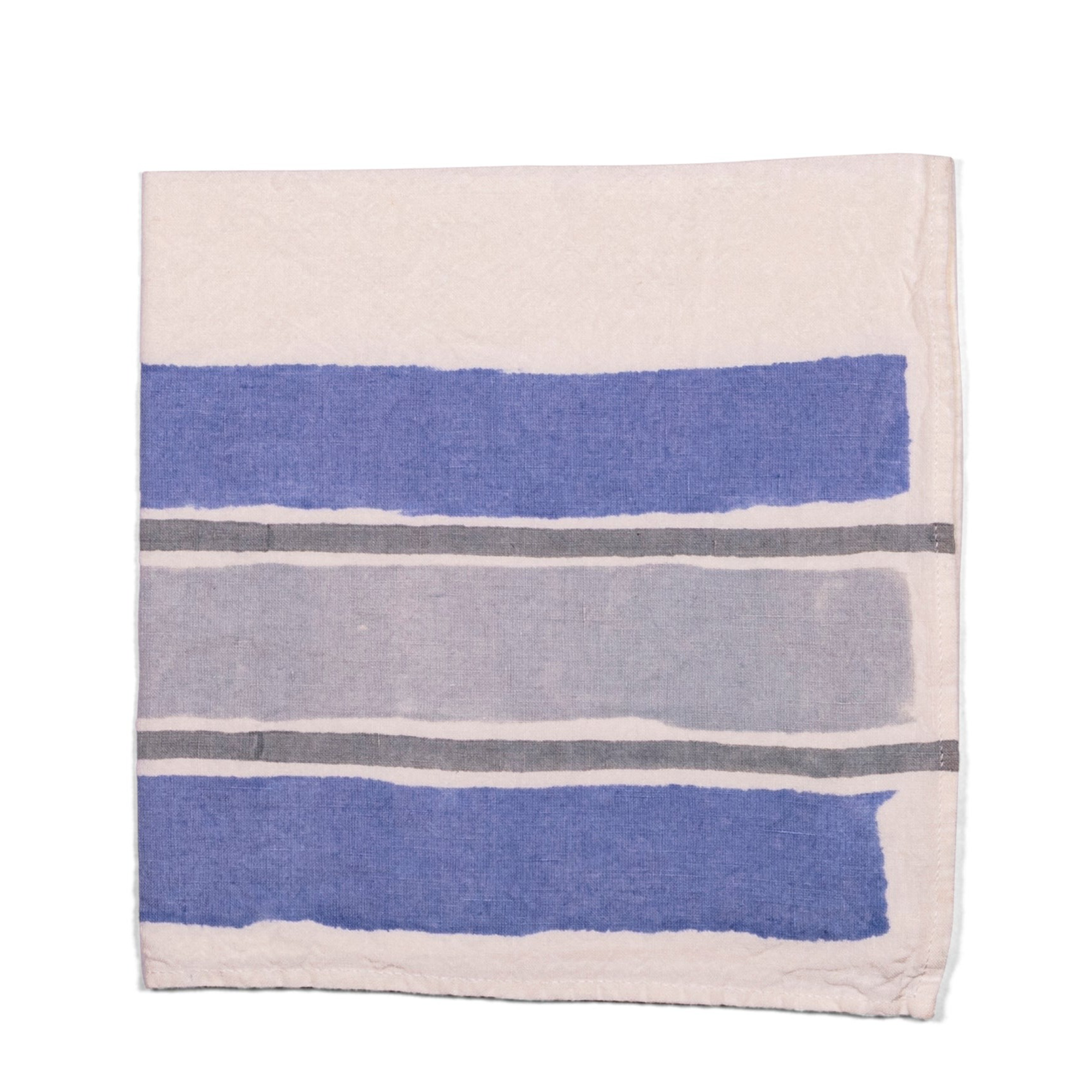 A 100% linen white napkin, with darker blue and grey stripes, handmade of pear wood. Perfect for breakfast, formal dining, or a garden tablescape.